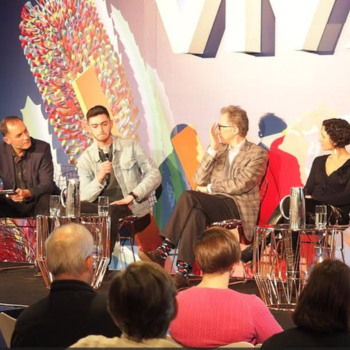 A panel of four speakers in conversation on a stage at a Vivid Sydney event, with a colourful illuminated backdrop and an audience in the foreground